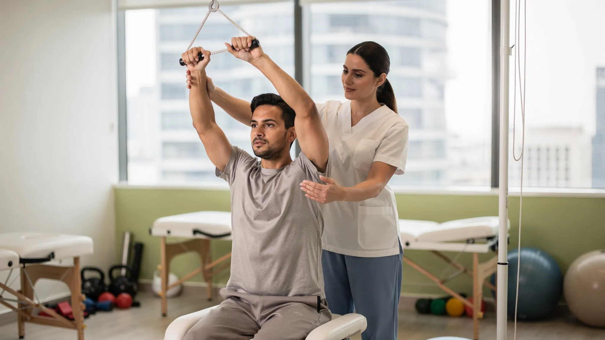 A patient performing supervised shoulder pulley exercises during post surgical rehabilitation, with a physiotherapist cueing scapular alignment and a clean therapy space in Dubai.